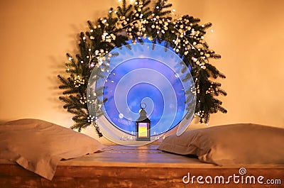 Christmas time. Vintage glowing lantern by round window decorated with tree branch and xmas lights Stock Photo
