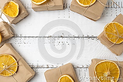 Christmas top view over a white wooden background with gift boxes packed in a craft paper with dryed oranges on top of it. Flat la Stock Photo