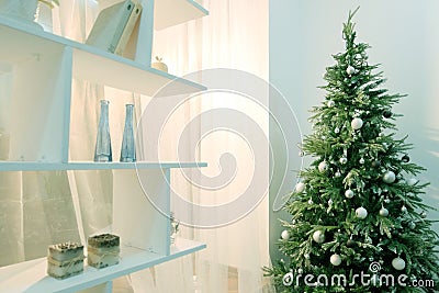 Christmas tree in the corner of the room next to a white rack with shelves. Modern decor in the house for the holiday. Abstract ba Stock Photo