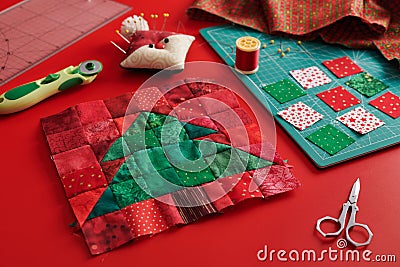 Christmas tree patchwork block, craft mat, bright square pieces of fabric, pincushion like Santa and quilting accessories on red Stock Photo