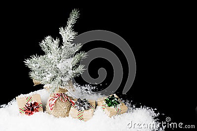 Christmas tree wrapped in burlap with simple holiday gifts wrapped in ribbon and shiny bows, covered in snow Stock Photo