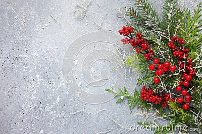 Christmas or winter background with a border of green and frosted evergreen branches and red berries on a grey vintage board. Flat Stock Photo