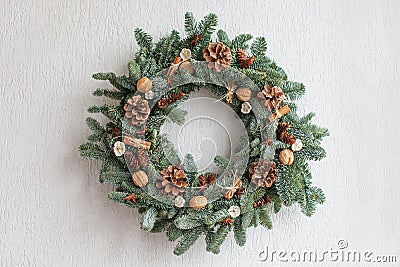 Christmas wreath made of natural fir branches hanging on a white wall. Wreath with natural ornaments: bumps, walnuts, cinnamon, Stock Photo