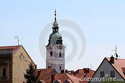 Church bell tower with analogue clocks on all sides and large metal cross on top rising high above city family houses rooftops Stock Photo