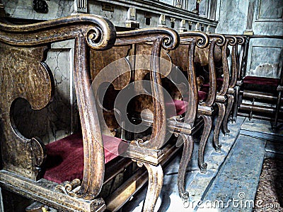 Church chairs or benches inside a church. The chairs are decorated with rich wood carvings and equipped with a soft seat of red Stock Photo