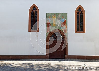 Church entrance with wooden door and religious mural, large historical stained glass windows, without people during the day Stock Photo