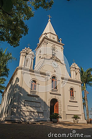 Church facade and belfry in front of a small cobblestone square with evergreen garden, in a sunny day at SÃ£o Manuel. Stock Photo