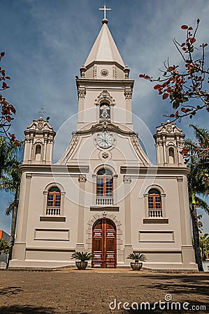 Church facade and belfry in front of a small cobblestone square with evergreen garden, in a sunny day at SÃ£o Manuel. Stock Photo