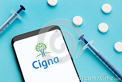 Cigna logo on Smart phone screen pills and syringe on blue background Editorial Stock Photo