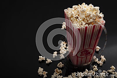 Cinema and movies concept with a box of popcorn and cinematography celluloid filmstrip rolling wround it with copy space Stock Photo