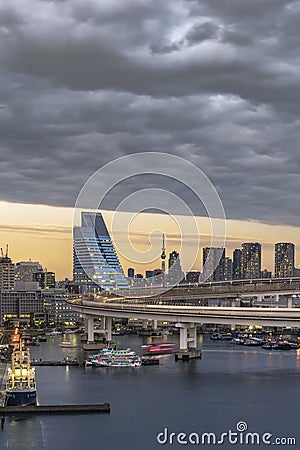Circular highway leading to the Rainbow Bridge with Cargo and cruise ships moored in Odaiba Bay of Tokyo Editorial Stock Photo