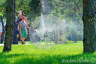 City park on a summer day, green lawns with grass and trees, paths and benches, people walking and children playing, bright Stock Photo