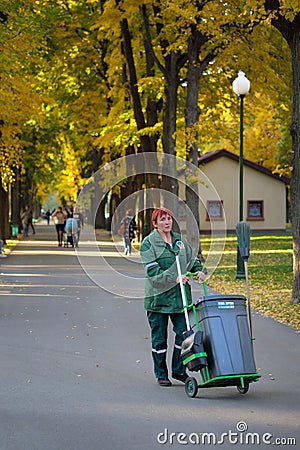 City park worker in a green suit with a garbage bin. Editorial Stock Photo