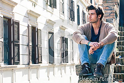 City young handsome man. Urban sitting model. Building windows Stock Photo