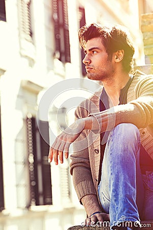 City young handsome man. Urban sitting model. Building windows Stock Photo