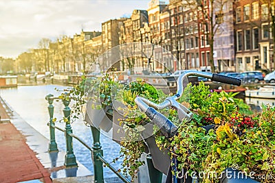 Cityscape on a sunny winter day - view on the parked bicycle with flowers on a canal background in the historic center of Amsterda Stock Photo