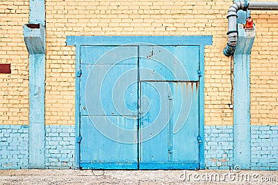 Cityscape. Urban symmetric view of abandoned factory building blue painted rusty gate on yellow brick wall with Stock Photo