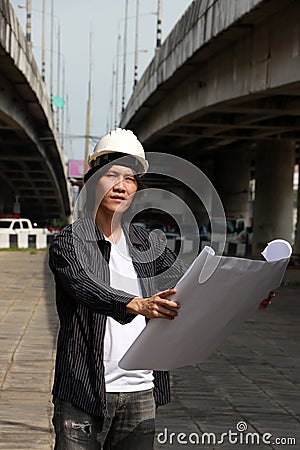 Civil engineer man with helmet, standing and looks at the project drafts while on parallel expressway background Stock Photo