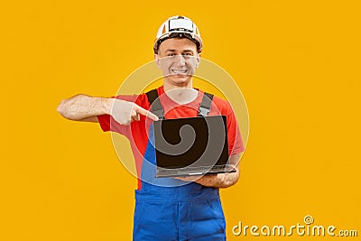 Civil engineer worker or builder wears helmet holds laptop with blank screen and points at it with index finger. Copy space, mock Stock Photo