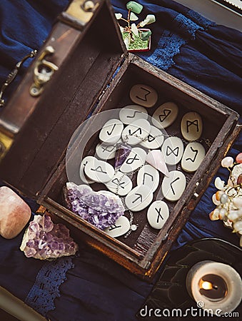 Clairvoyant tools rune stones, crystal pendulums in natural dark wooden case box on dark blue background. Stock Photo