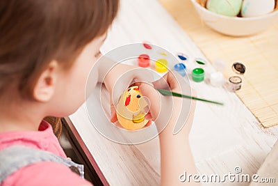 The girl paints the egg at the table at home Stock Photo