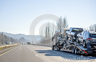 Classic bonnet big rig car hauler semi truck transporting cars on semi trailer running on the intestate wide highway Stock Photo