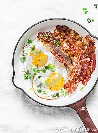 Classic Breakfast - fried eggs and bacon in a cast iron pan on a light background Stock Photo