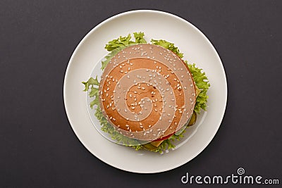 Classic burger served on white plate over black background. Meat hamburger flat lay. Junk food, fast food concept. Stock Photo