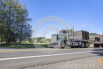 Classic compact powerful old style green big rig semi truck transporting fastened cargo on flat bed semi trailer running on the Stock Photo