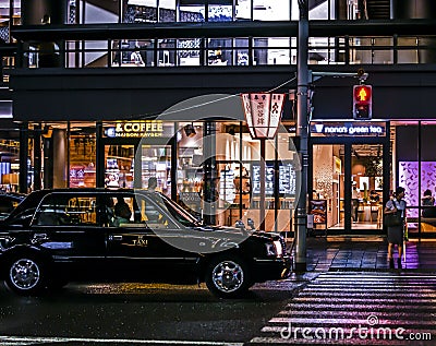 Classic japanese taxi in front of a pedestrian crosswalk and a few shops. Night photography Editorial Stock Photo