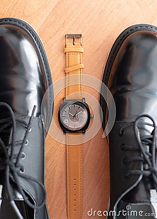 Classic mechanical wrist watch lay between pair of man black formal shoes. top view Stock Photo