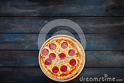 Classic pepperoni pizzai on a wooden stand on a dark wooden background. Top view bottom orientation Stock Photo