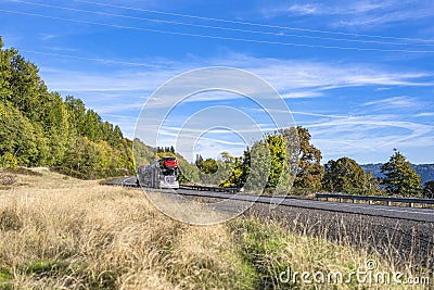 Classic powerful car hauler transporting cars on two level modular semi trailer running on the winding road with dry grass and Stock Photo