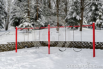 Classic swing set in a public park, red support stand and black rubber regular and baby swing seats, snowy day Stock Photo