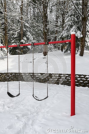 Classic swing set in a public park, red support stand and black rubber swing seats, snowy day Stock Photo