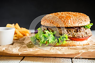 Classic tasty hamburger with tasty beef, sauce and french fries on dark background. American food Stock Photo