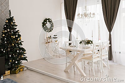 Classic white living room or dining room with a wooden white table and chairs, a Christmas tree and brown curtain Stock Photo