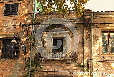 Classic wide-angle view of the facade of the abandoned building. Old windows with the wooden shutters. Weeds growing on the wall. Stock Photo