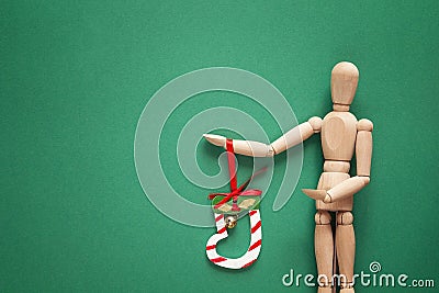 Classic wooden dummy holds Christmas bell on a green background. Stock Photo