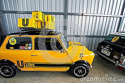 Classic yellow Mini Austin car is pictured parked in a garage, with a black wheel and a yellow box Editorial Stock Photo