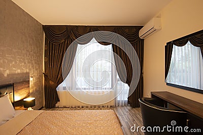 Classy bedroom interior design. Large bed. Room with brown color tone furniture. Windows with long curtains, drapery and sheers. Stock Photo