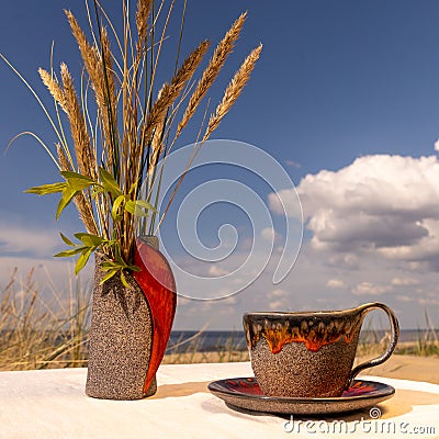 A clay ceramic vase and a cup with a saucer placed on a linen tablecloth on the sea beach...The lower parts of the vase and mug Stock Photo