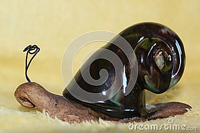 Clay decorative snail with enamel dark paint on his shell, wires as antennae, placed on yellow fluffy blanket. Stock Photo