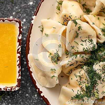 Clay plate of boiled dumplings sprinkled with dill herbs and ghee on black table background. High angle view. Cooking Stock Photo