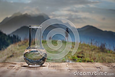 Clean water in a glass laboratory flask on wooden table on mountain background. Ecological concept, the test of purity Stock Photo