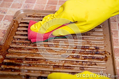 Cleaning the grill. Hands in yellow gloves clean the dirty grill of grease and burns with a cleaning agent. electric grill hygiene Stock Photo