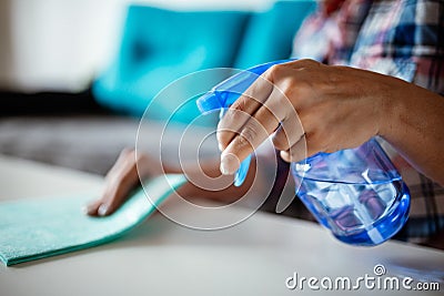 Cleaning home surface with sponge and spray cleaner. Female hands using spray cleaner on white table. Maid wiping dust while Stock Photo