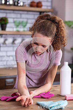 Disquieted light-haired girl leaning on kitchen table and inspecting Stock Photo