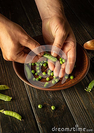Cleaning peas after harvest. Close-up male hands are peeling peas into a plate. Vegetarian food preparation Stock Photo