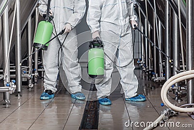 Cleaning of production. Guys in hazmat suits disinfect equipment Stock Photo